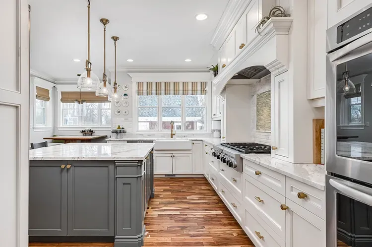 White kitchen cabinets with a gray island and brass pulls refinished by Elegant Edge Painting.