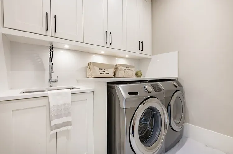 White laundry room cabinets above a sink and washer refinished by Elegant Edge Painting.