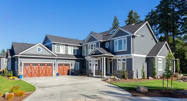 Two-story blue-gray craftsman home with white trim and wood garage doors after an exterior repaint by Elegant Edge Painting.