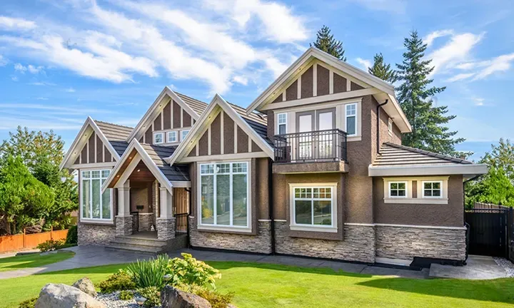 Brown stucco home with cream trim and a stone base after an exterior repaint by Elegant Edge Painting.