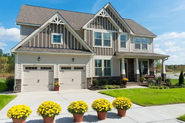 Two-story home with gray board-and-batten gables and white garage doors after an exterior repaint by Elegant Edge Painting.
