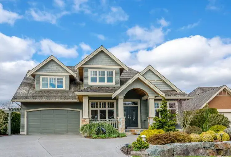Sage green shingle-style home with cream trim and a stone entry after an exterior repaint by Elegant Edge Painting.