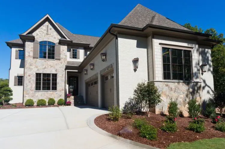 Stone and white-painted brick home with dark window trim after an exterior repaint by Elegant Edge Painting.