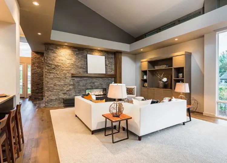Vaulted living room with white walls, a charcoal accent ceiling, and a stacked stone fireplace after an interior repaint by Elegant Edge Painting.
