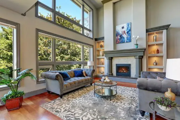 Two-story living room with greige walls and lit built-in shelves beside the fireplace after an interior repaint by Elegant Edge Painting.
