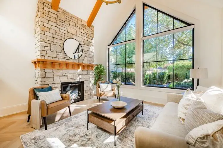 Vaulted living room with cream walls, a stone fireplace, and large black-framed windows after an interior repaint by Elegant Edge Painting.