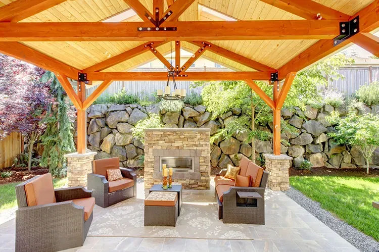 Cedar pergola with stained beams over an outdoor fireplace patio, with a fresh stain by Elegant Edge Painting.